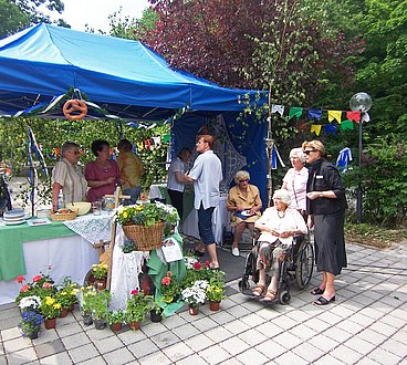 Bewohnerinnen des Haus am Urselbach bei einem Fest, vor einem Pavillon mit Buffet, das mit vielen Blumen verziert ist