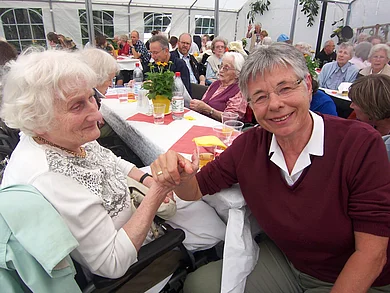 Bewohnerin des Haus am Urselbach, in einem gefüllten Festzelt, gemeinsam mit einer ehrenamtlichen Mitarbeiterin am Tisch sitzend