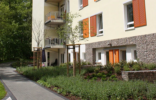 Haus am Urselbach mit Balkons, kleinem Garten und barrierefreiem Zugangsweg durch eine begrünte Anlage